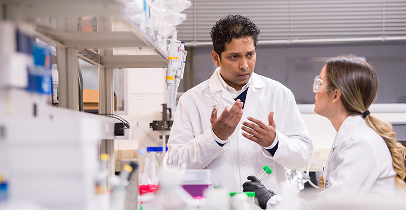 Two people in lab coats having a discussion in a lab. 