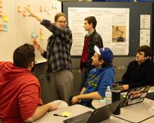 Students gather around a whiteboard adding ideas to post-its