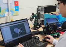 Person using a laptop to program and test a small robotic vehicle in a technology lab