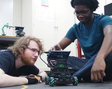 Two students sit on the floor programming a robot
