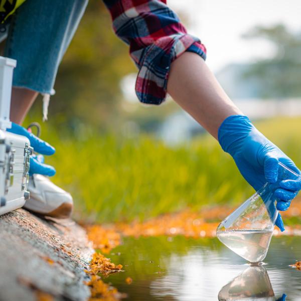 A person gathering water from an outdoor water source into a flask.