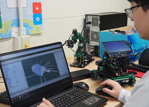 Person using a laptop to program and test a small robotic vehicle in a technology lab.